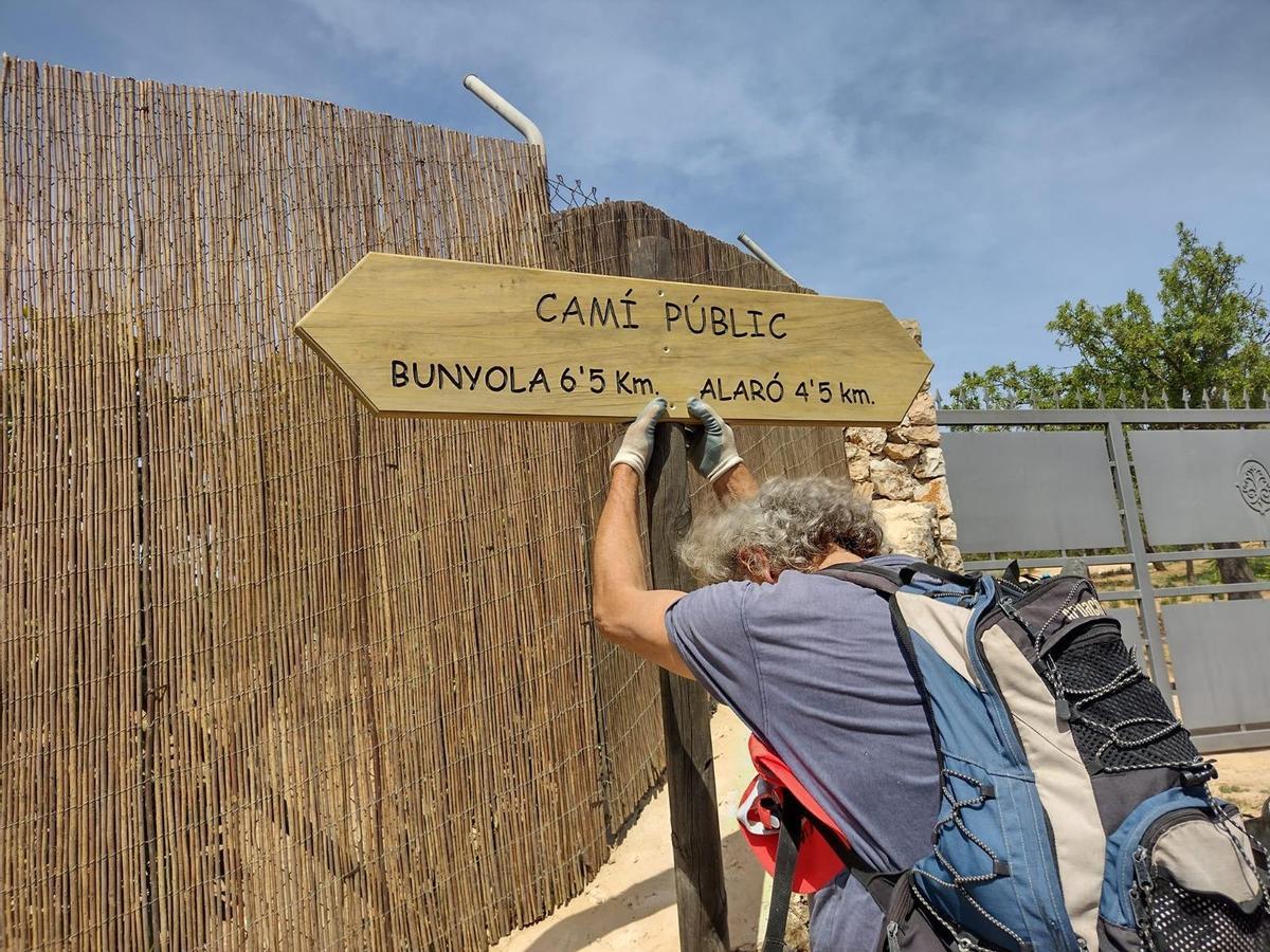 Un activista coloca un cartel del camino público junto a una de las barreras que impiden el paso.