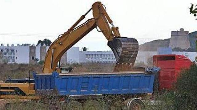 Una pala excavadora carga un camión con tierra acumulada en Platja d'en Bossa.