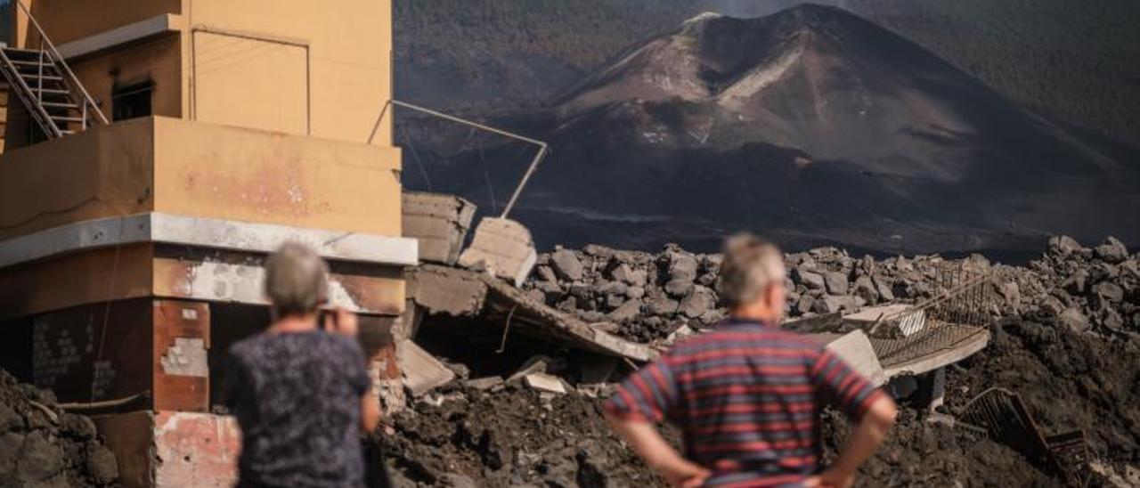 Dos personas observan el volcán de Tajogaite y sus efectos sobre las viviendas que la lava arrasó a su paso.