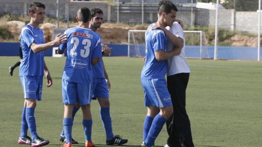 El capitán del Atlético Isleño Javi Escandell, en primer plano con rostro serio, se abraza con un compañero al finalizar el encuentro ayer en Can Misses.