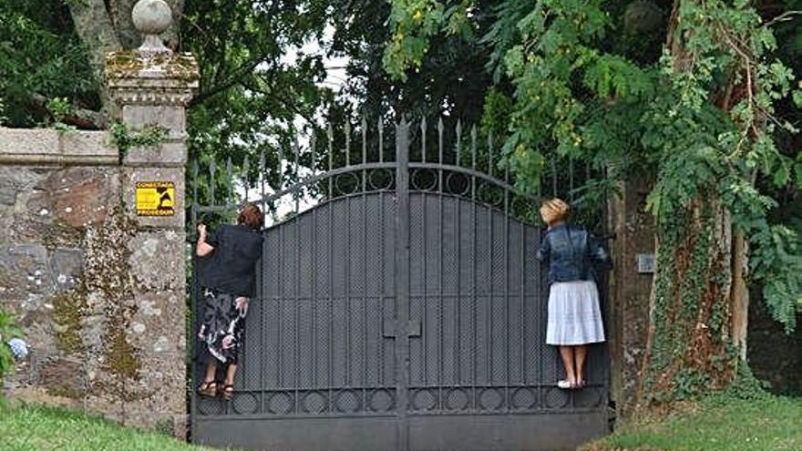 Dos mujeres encaramadas al portalón de entrada del pazo de Meirás.