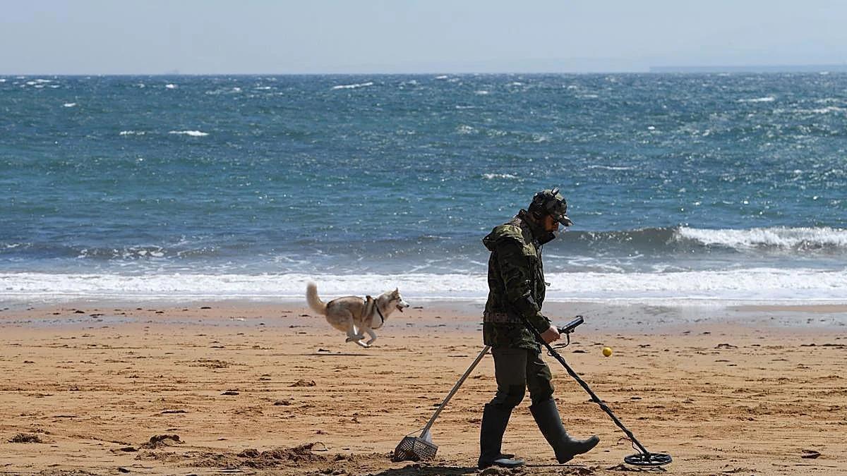Un hombre busca objetos en una playa con un detector de metales.