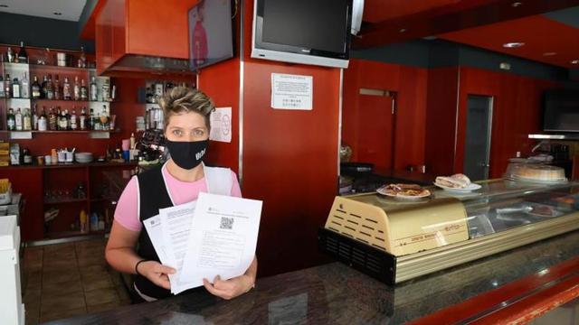 Rosa María Núñez, camarera en Cafetería Urbe, muestra algunos de los certificados necesarios para entrar al local.  |  // ALBA VILLAR