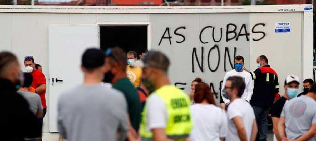 Trabajadores en la entrada de San Cibrao, ayer, donde puede leerse 'As cubas non se paran'.