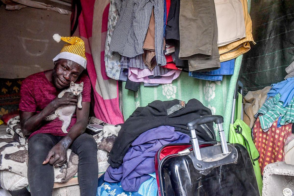 Moussa acaricia a su gata en el interior de la chabola en la que reside en la trasera  del mercado de Maspalomas.
