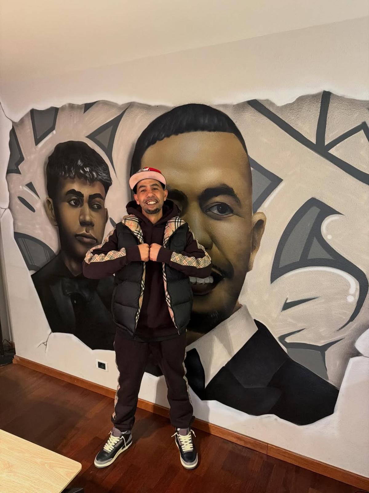 Mounir Nasraoui posando delante del mural que tiene en su casa