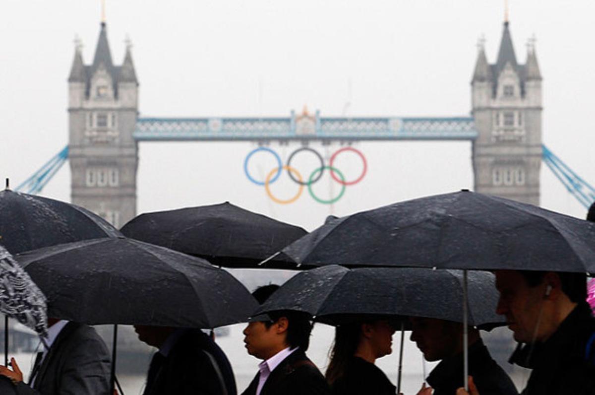Un grup de vianants caminen pel pont de Londres, amb els anells olímpics al fons, mentre la Gran Bretanya es prepara per a l’amenaça de pluges.