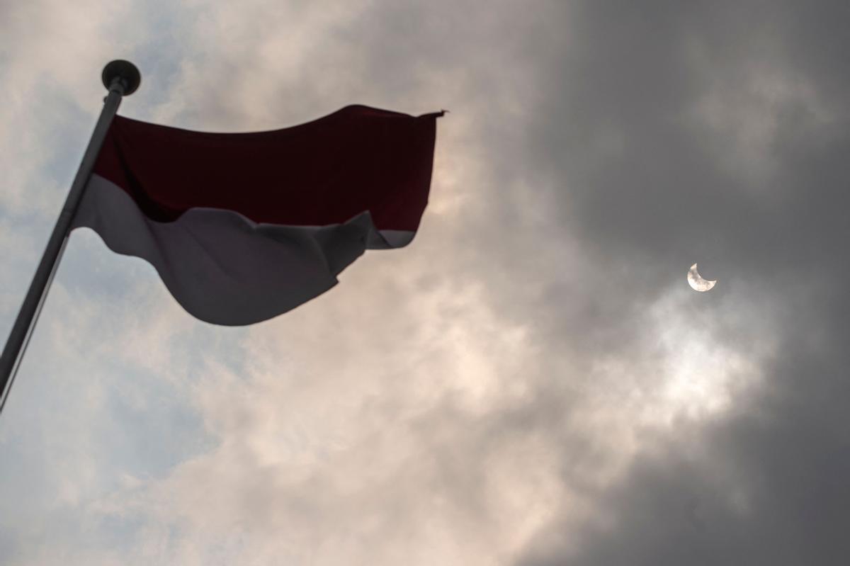 La bandera indonesia ondeando y, al fondo, el eclipse, en Surabaya.