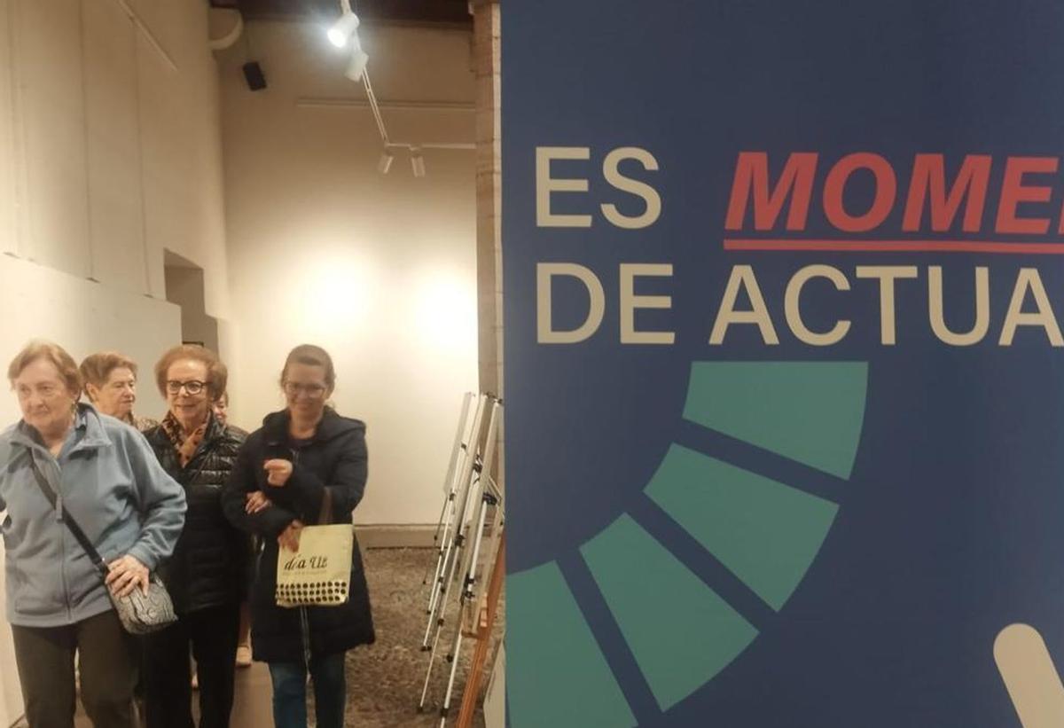 Un grupo de mujeres camina junto al cartel de la exposición de la Casa de Cultura de Grado. | SARA ARIAS