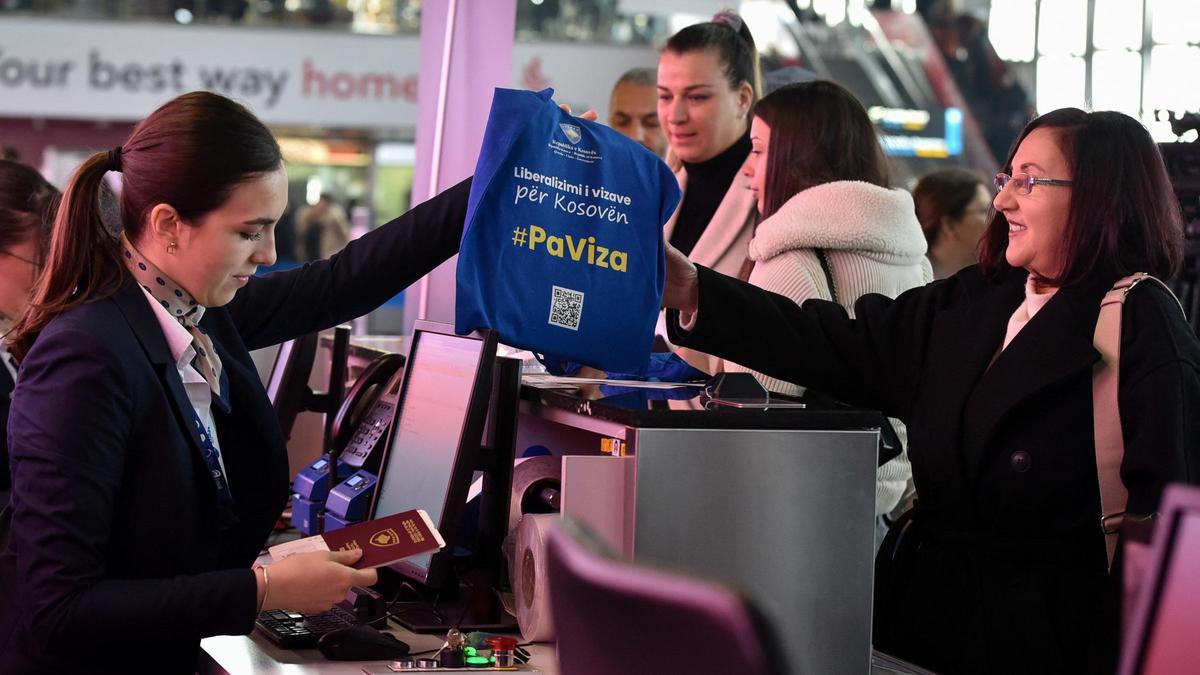 Una trabajadora del aeropuerto de Pristina entrega a una pasajera una bolsa con el mensaje &quot;SinVisado&quot;, este lunes.