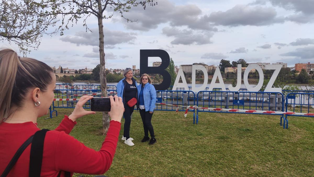 Dos personas se fotografían ante las grandes letras con el nombre de Badajoz colocadas en el parque de la margen derecha del río.