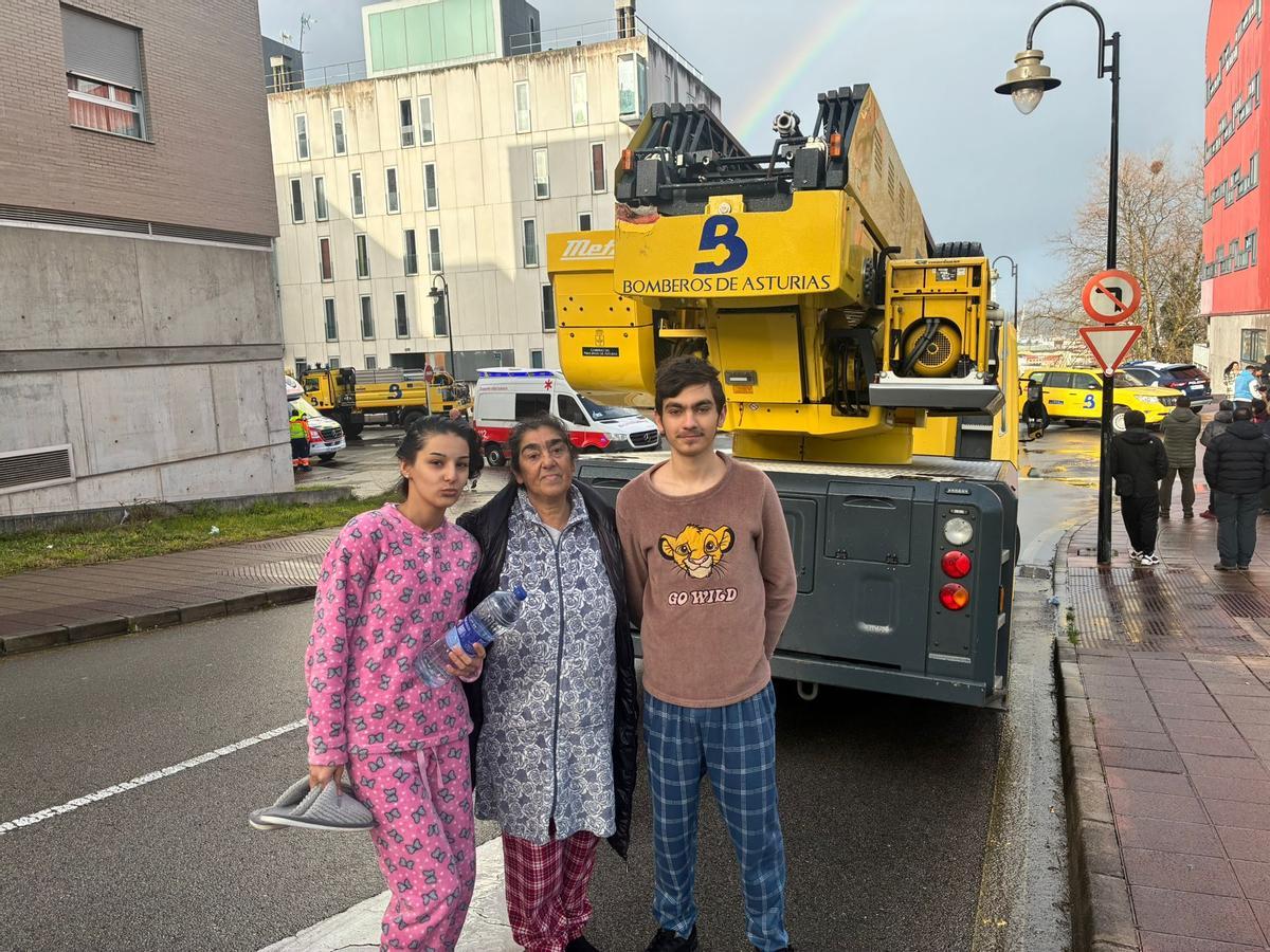 Damaris Pérez y José Jiménez con su abuela Adoración Jiménez, esta tarde, en el Nodo; al fondo, el edificio afectado y los vehículos de protección.