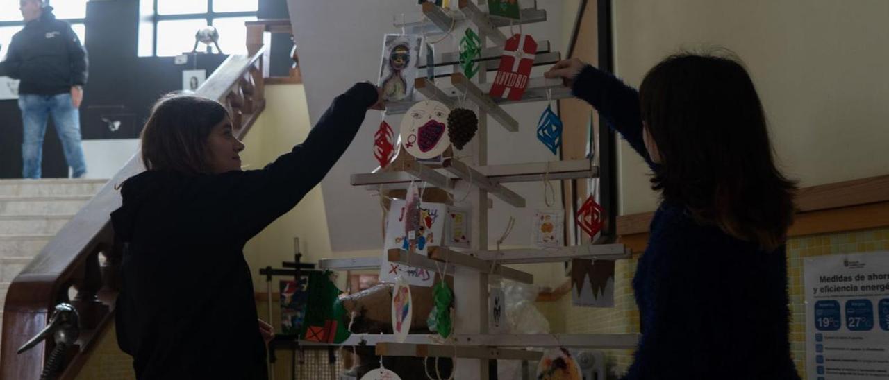 Arriba, dos estudiantes colocan postales en el árbol de madera. Abajo, la vidriera navideña, vista por dentro y por fuera del edificio. | Jose Luis Fernández
