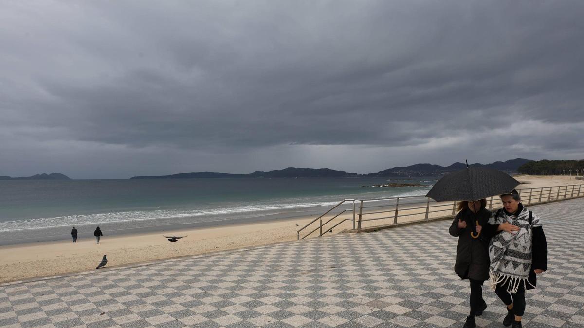 Dos personas se protegen de la lluvia con su paraguas en el paseo de Samil.