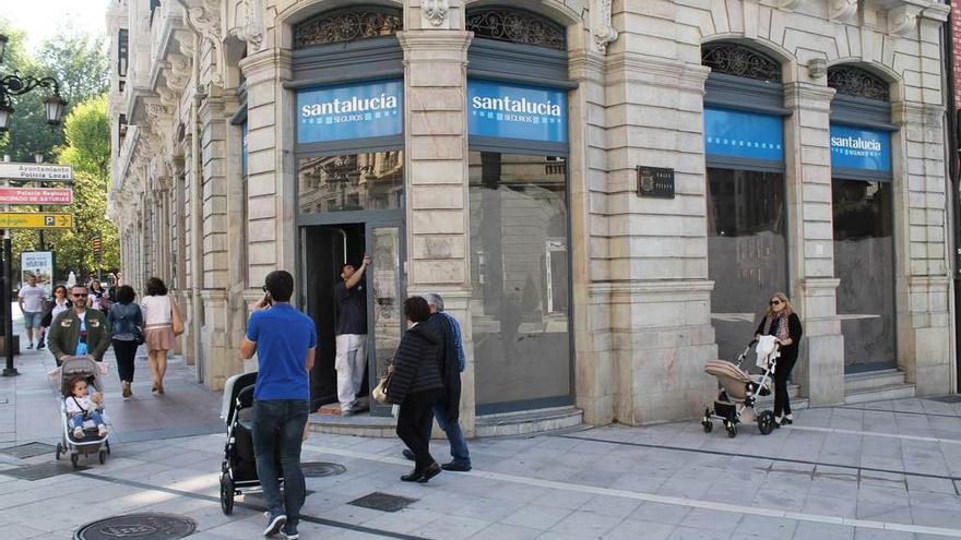 Un operario coloca la puerta del local del futuro Starbucks de Oviedo mientras pasan varios peatones.