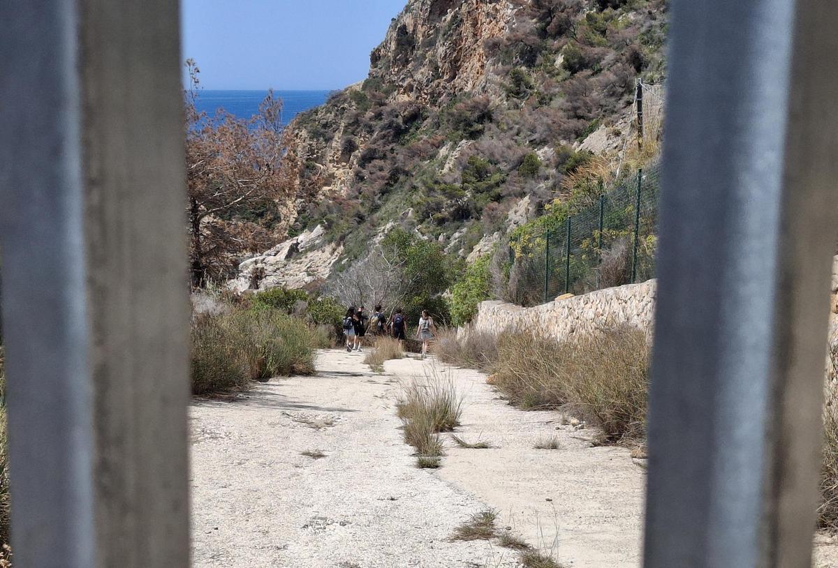 Un grupo de bañistas baja hacia la cala tras sortear el portón de hierro