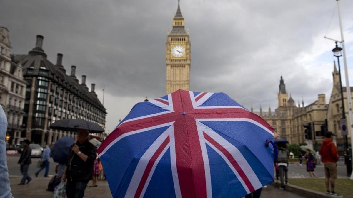 Un transeúnte se refugia de la lluvia en un paraguas con la bandera británica, cerca del Big Ben, este sábado.