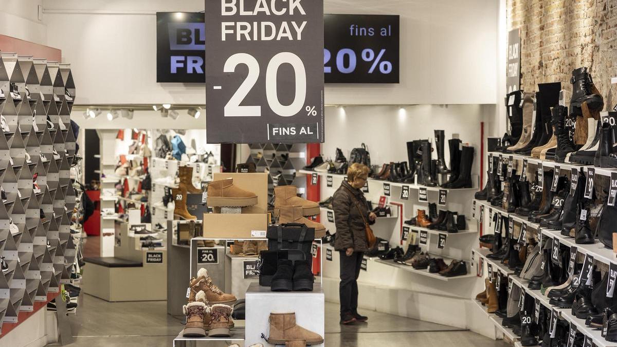 Una mujer observa zapatos en una tienda con una promoción del 20% de descuento la tarde antes del Black Friday oficial