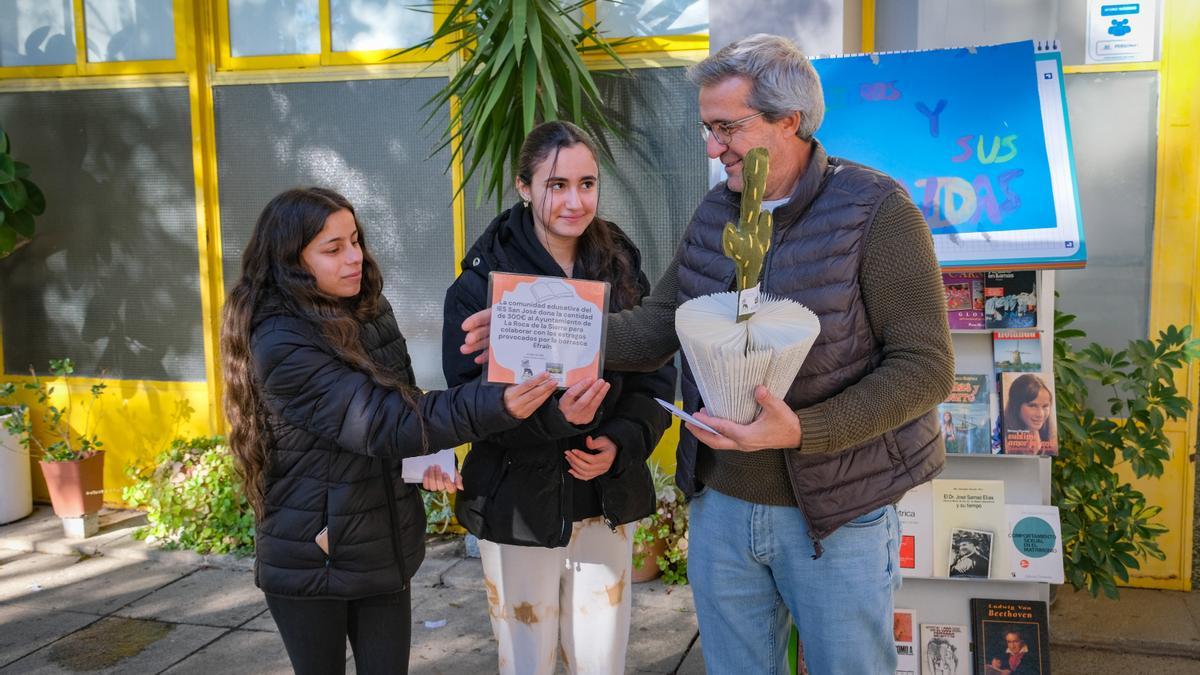 Dos alumnas del centro le dan al alcalde el cheque para ayudar a la localidad.