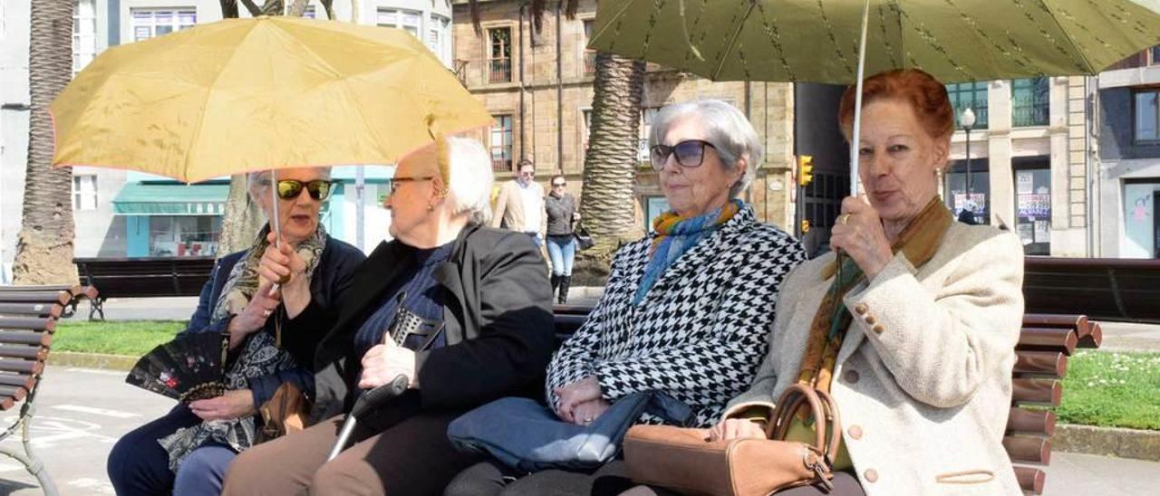 Unas señoras se protegen del sol con paraguas sentadas en un banco de los Jardines de la Reina.