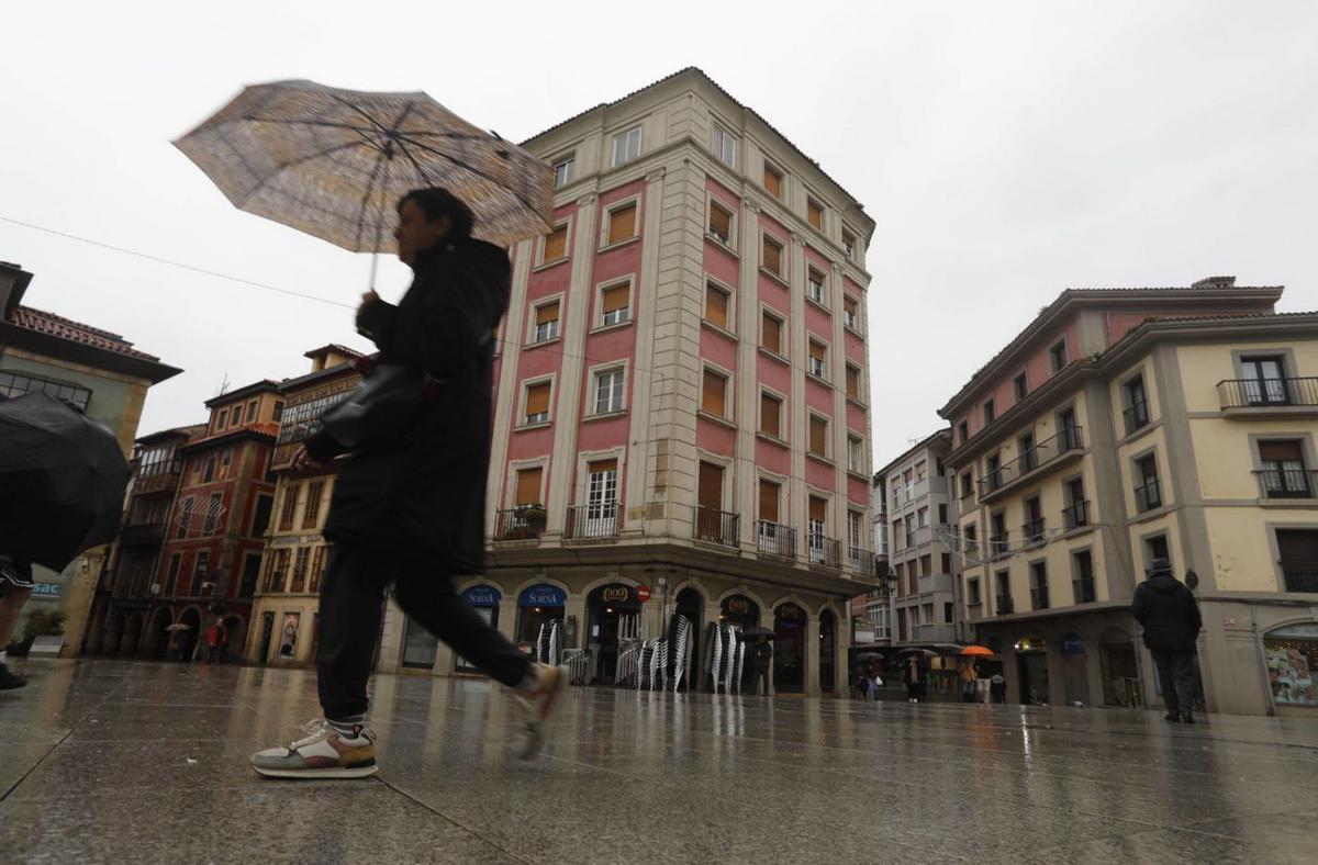 Varios paseantes bajo la lluvia, ante el edificio de Precios Únicos, que se transformará para albergar un total de 31 apartamentos turísticos. | LNE