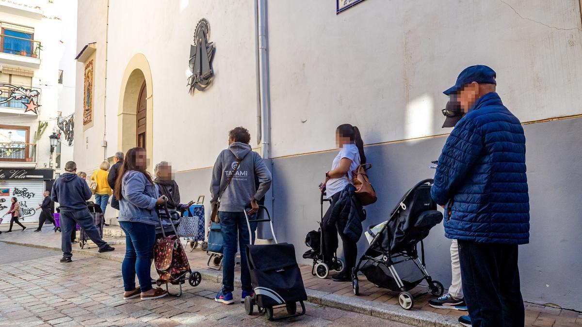 Varias personas hacen cola para recibir alimentos y ropa en una parroquia.