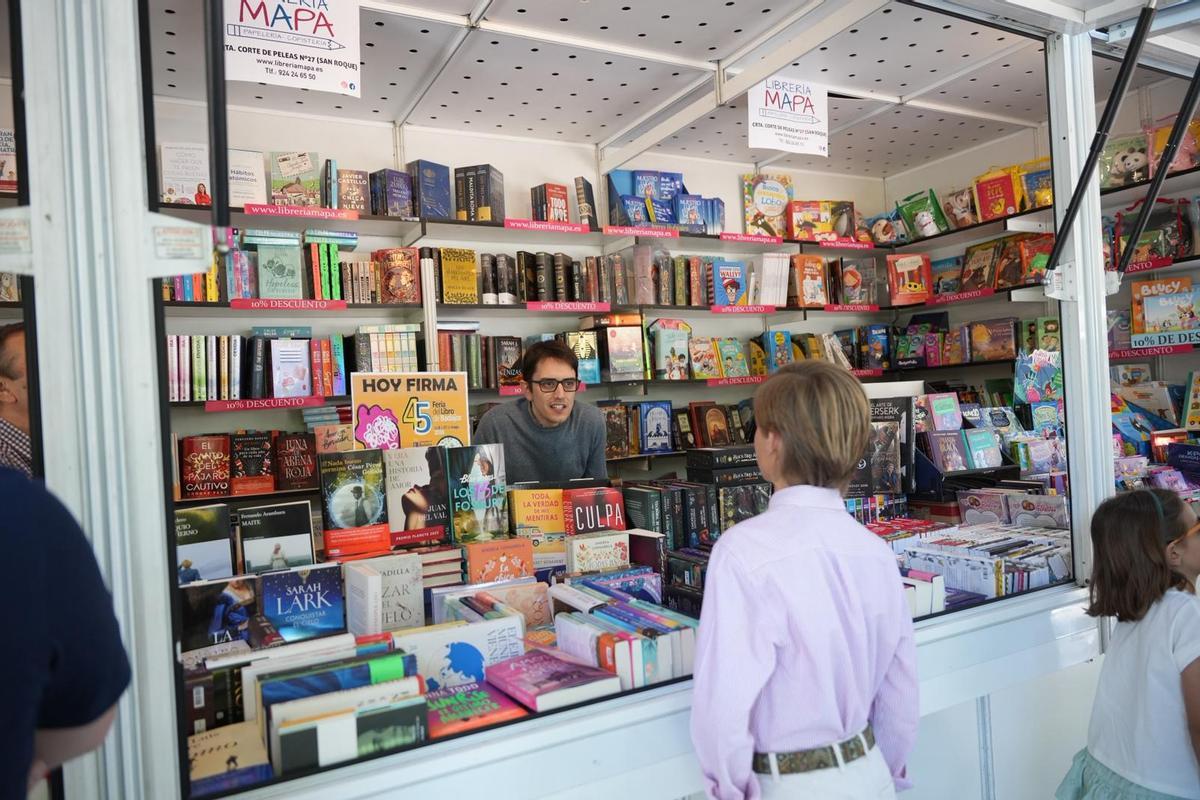 Álvaro Resina, de la Librería Mapa, atiende a un niño en la Feria del Libro de Badajoz 2026.