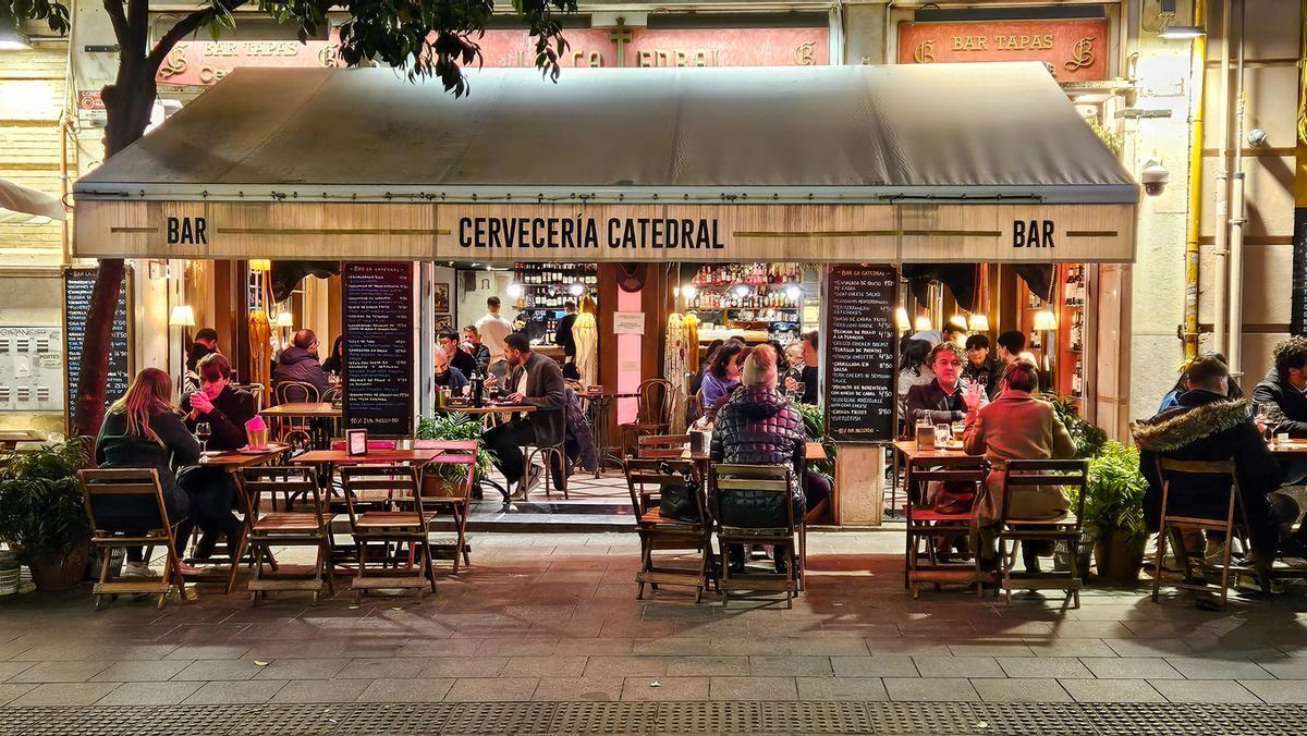 La cultura callejera española, la vida nocturna, la gente sentada en las mesas del bar callejero "Cervecería Catedral" cerca de la plaza central de la Giralda.
