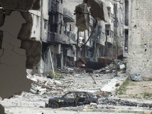 A damaged car is seen near carpets erected as protection from snipers along a street at the al-Bayada district of Homs