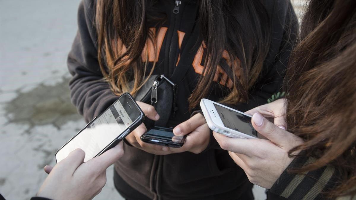 Unas adolescentes usan sus teléfonos móviles en la puerta de Apple de Barcelona, en enero del 2018