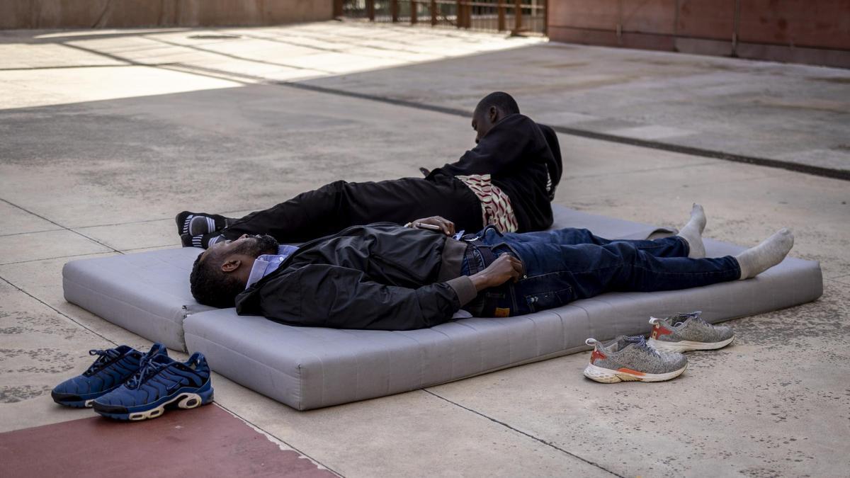 Dos migrantes sin hogar descansan en un colchón frente al Centro de Historias de Zaragoza, este martes.
