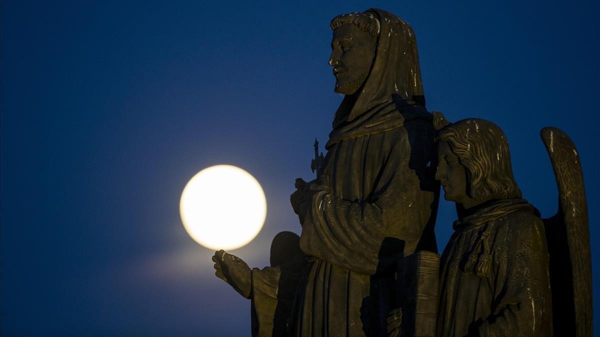 La superluna rosa, tras una de las estatuas del Puente Carlos de Praga, en la República Checa, este lunes.