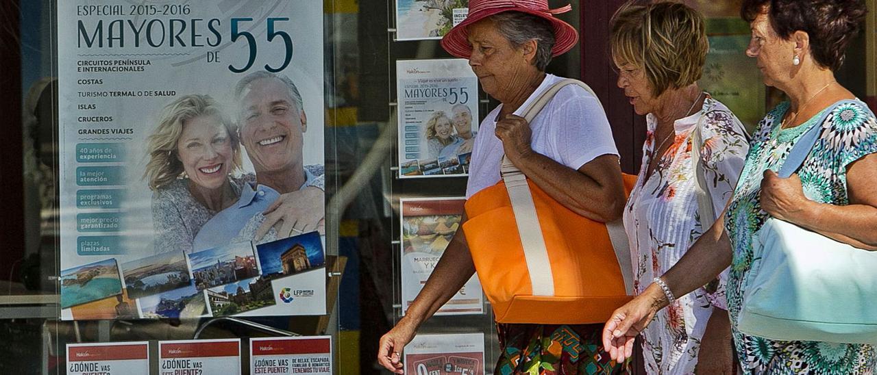 Tres mujeres pasan junto al escaparate de una agencia donde se ofertan viajes para mayores de 55 años en una imagen de archivo.