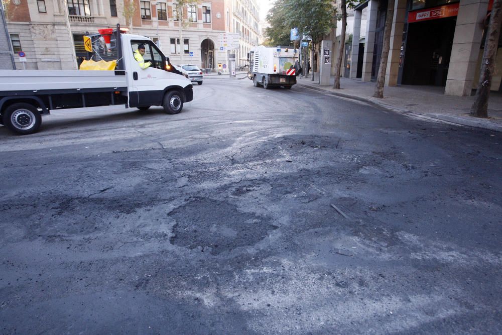 Carrers amb restes de mobiliari urbà cremat, contenidors per terra i treballadors de la brigada treballant