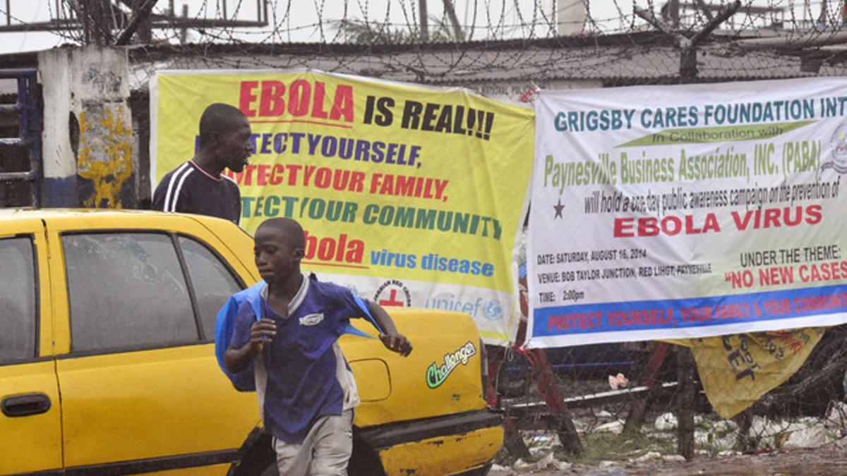 Transeúntes pasan frente a un cartel que alerta del riesgo del ébola en Monrovia, este domingo.