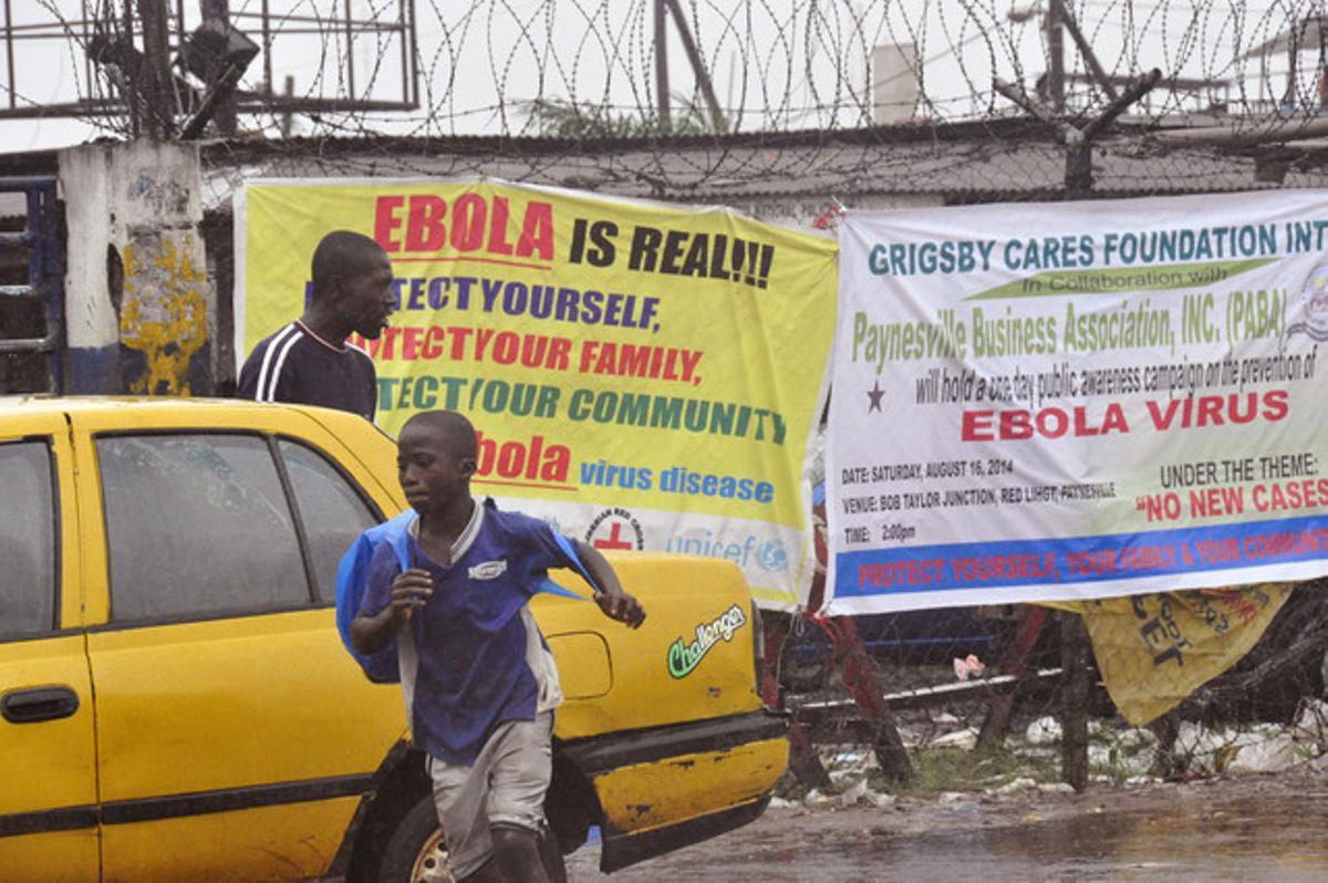 Transeünts passen davant un cartell que alerta del risc de l’Ebola a Monròvia, aquest diumenge.