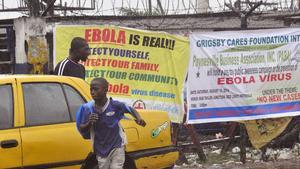 Transeünts passen davant un cartell que alerta del risc de l’Ebola a Monròvia, aquest diumenge.
