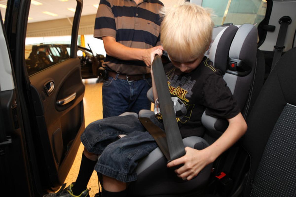 Un nen amb una cadira reglamentària s’estreny el cinturó de seguretat.