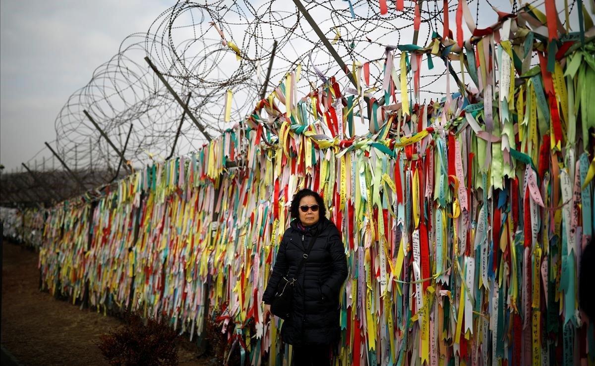 Una mujer posa frente a una cerca de alambre de púas decorada con cintas con mensajes que desean la unificación de las dos Coreas, cerca de la zona desmilitarizada que las separa, en Paju.