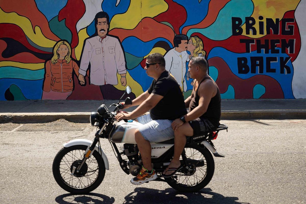 Dos jóvenes pasan en moto frente a un mural en honor a Nicolás Maduro y Cilia Flores en Catia la Mar
