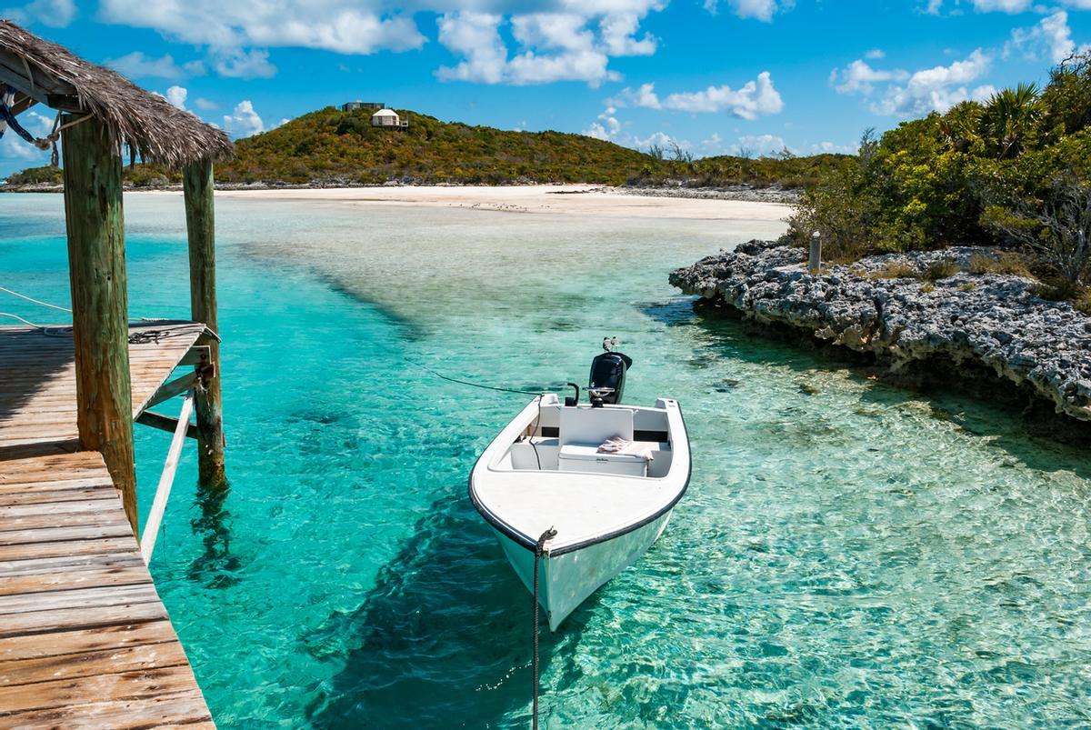 Pequeño barco amarrado de un muelle sobre aguas del océano turquesa cerca de las remotas islas Exuma en las Bahamas