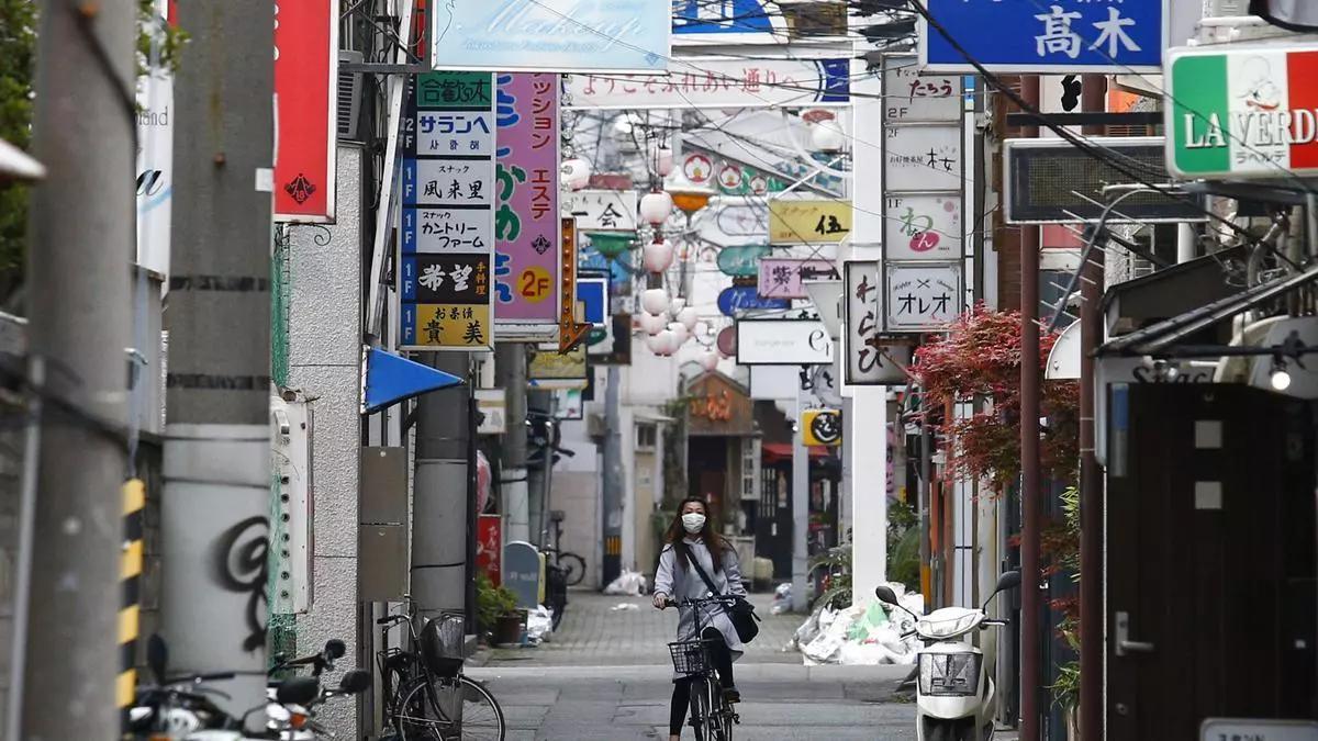 Una mujer con mascarilla recorre en bicicleta una calle de Tokio.