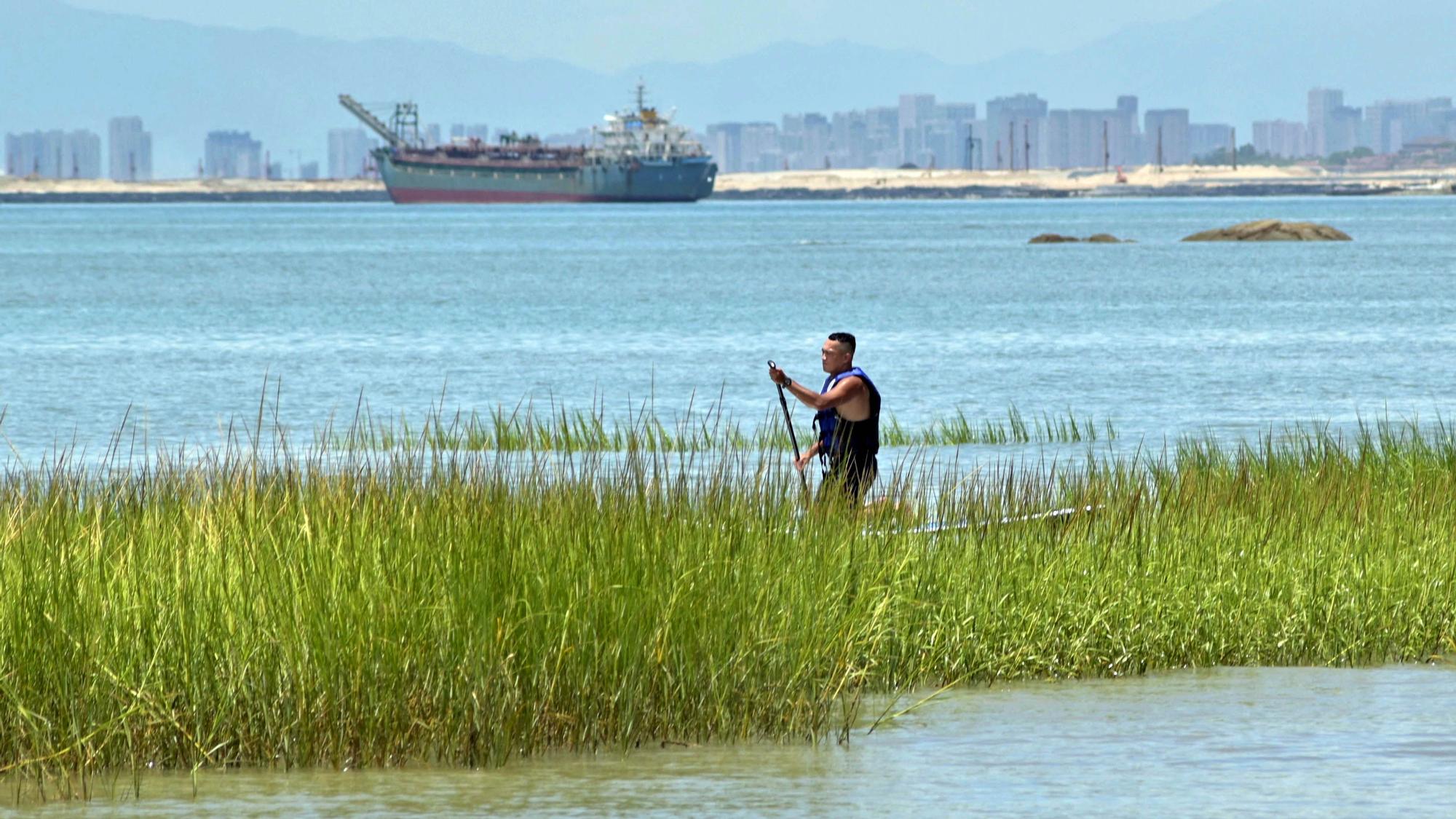 Un hombre rema entre juncos mientras se ve el horizonte de la ciudad de Xiamen en la parte continental de China desde las islas Kinmen de Taiwán, que se encuentran a solo 3,2 km  de la costa de China continental