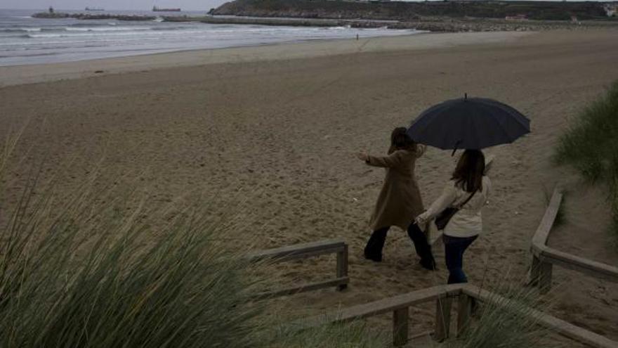 Dos jóvenes, ayer, en la playa de San Juan; a la derecha, el espigón construido en 2004 y que el PP sopesa ampliar.