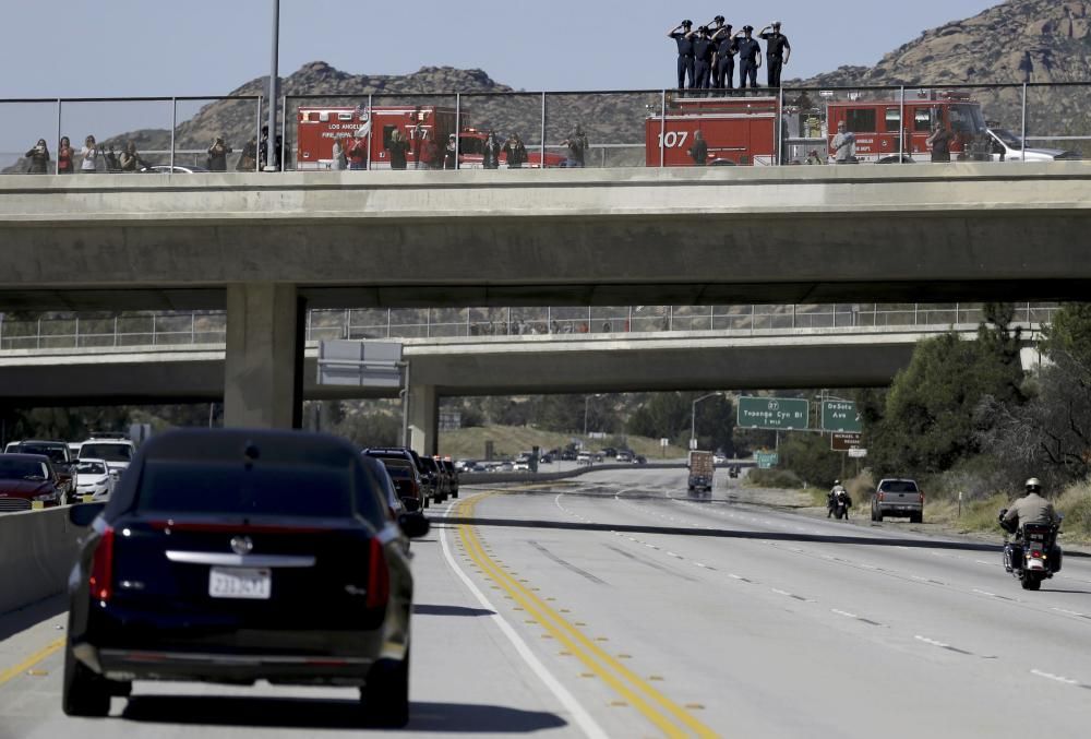 Firefighters stand on the roof of their vehicle ...