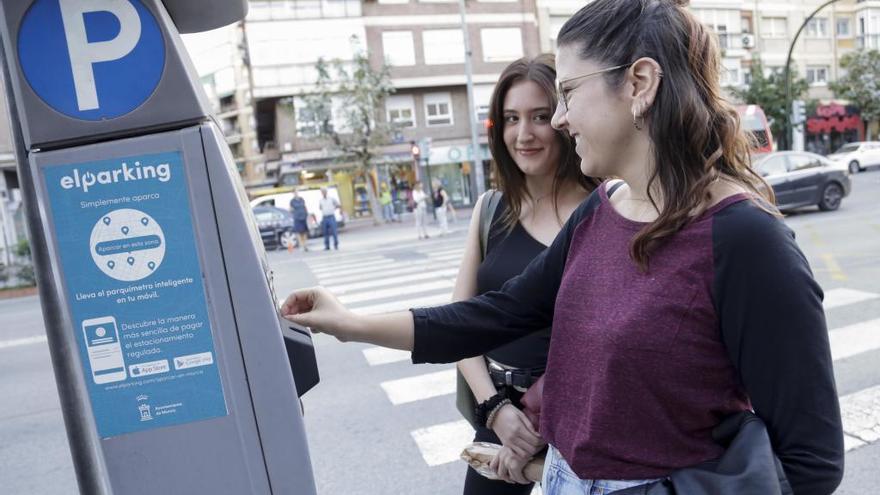 Dos jóvenes revisan la máquina de la ORA en Murcia.