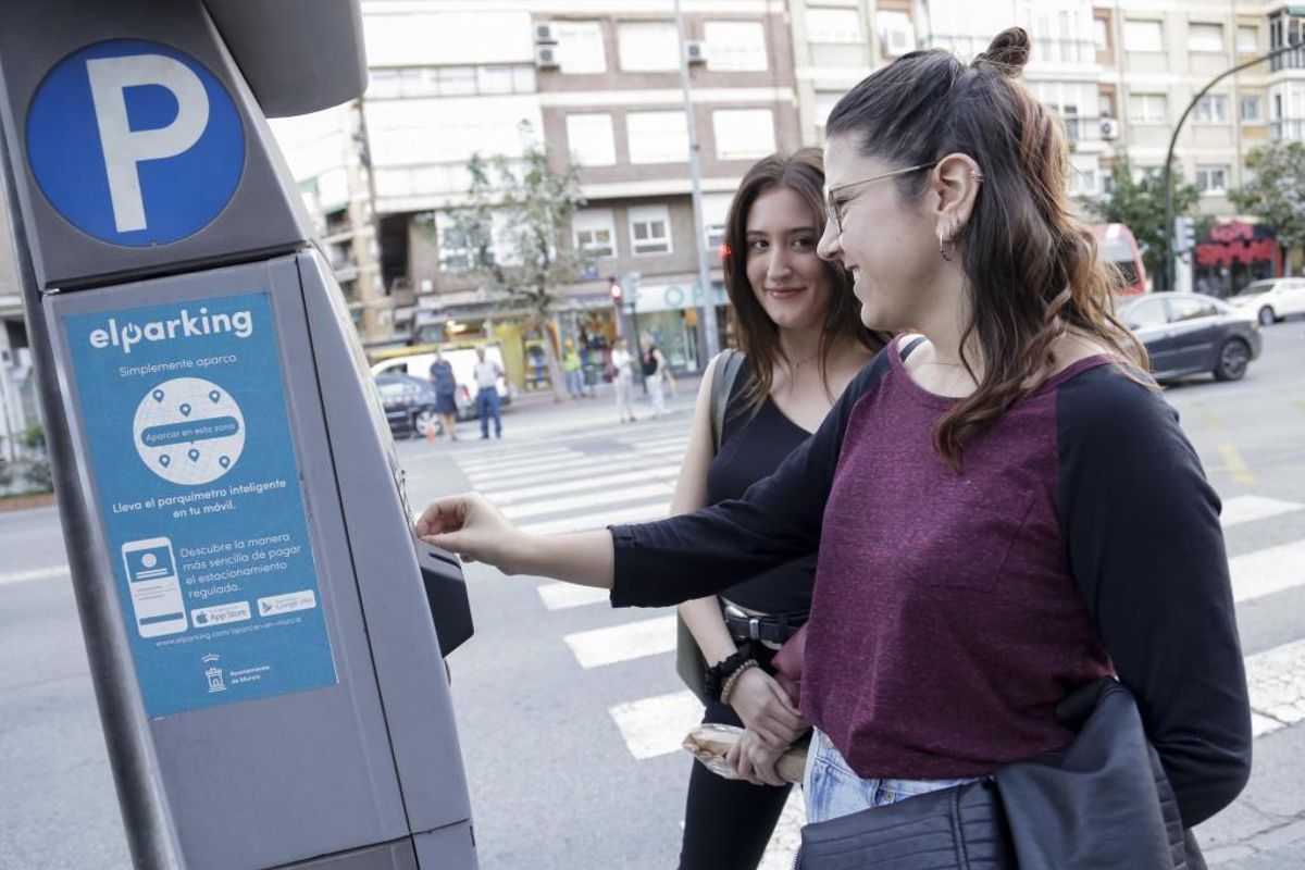 Dos jóvenes revisan la máquina de la ORA en Murcia.