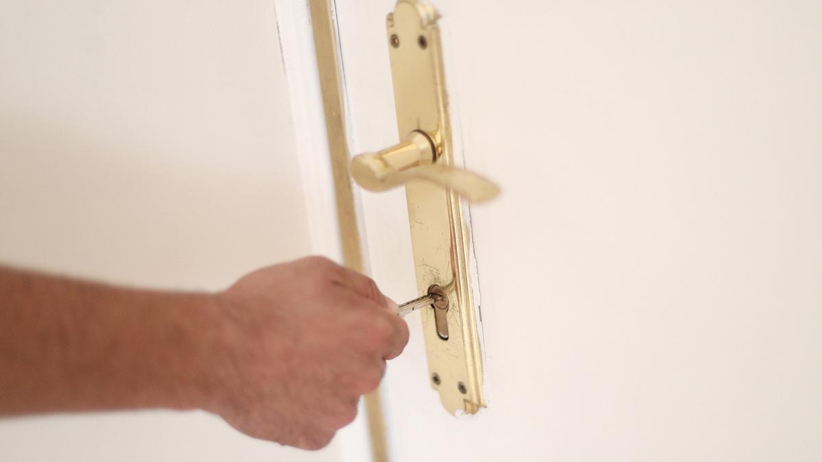 Un hombre introduce una llave en la cerradura de la puerta de una vivienda.