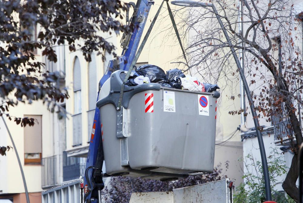 Carrers amb restes de mobiliari urbà cremat, contenidors per terra i treballadors de la brigada treballant