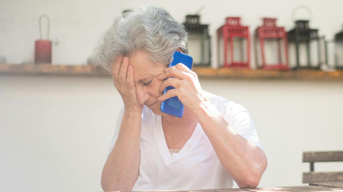 Una mujer mayor habla por teléfono con ademán preocupado.
